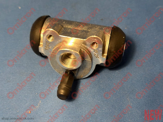 A new metal automotive brake master cylinder with black rubber boots on both ends, resting on a blue textured surface.