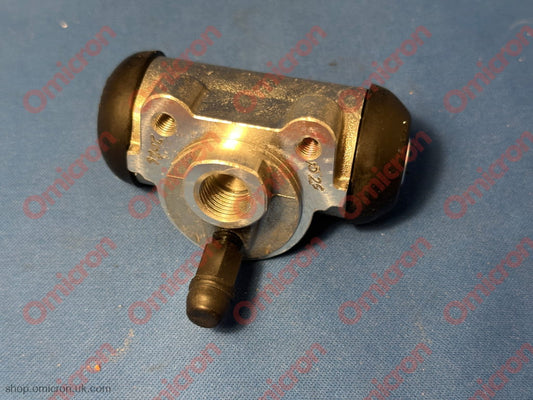 A new metal automotive brake master cylinder with black rubber boots on both ends, resting on a blue textured surface.